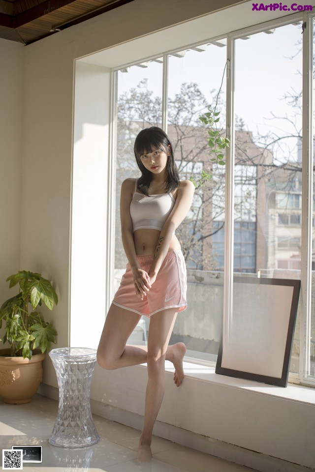 A woman standing in front of a window next to a plant.