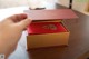 A person opening a red and gold box on a table.