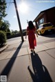 A woman in a red dress walking down a sidewalk.