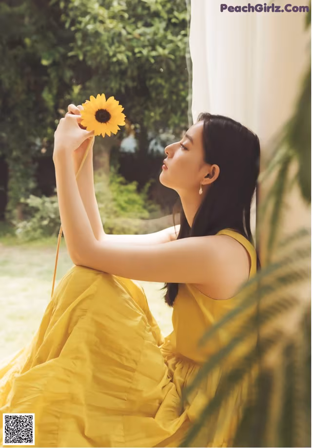 A woman in a yellow dress holding a sunflower.