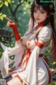 A woman in a white and red traditional outfit with a bow, sitting outdoors with greenery.