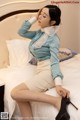 A woman sitting on top of a bed wearing a blue shirt and skirt.