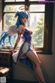 A woman with blue hair and angel wings leaning against a window.