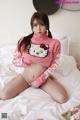 A woman in a pink sweater sitting on a bed.