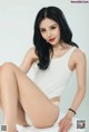 A woman in a white tank top sitting on a white table.