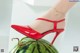 A woman wearing a pair of red high heels on top of a watermelon.