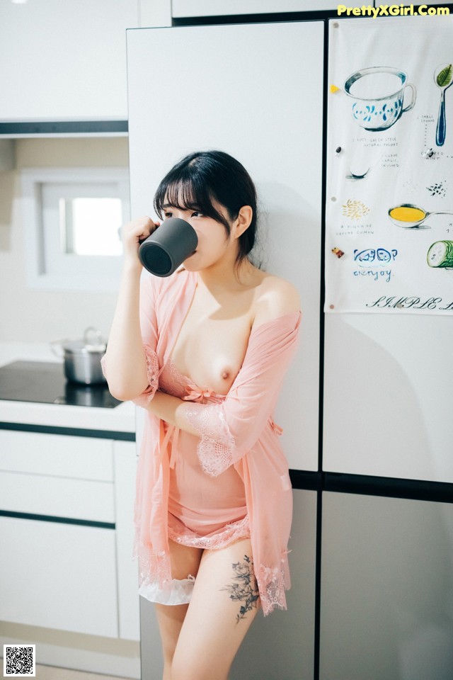 A woman in a pink robe drinking from a cup.