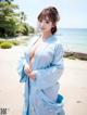 A woman in a blue kimono standing on a beach.