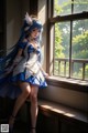 A woman in a blue and white dress standing by a window.